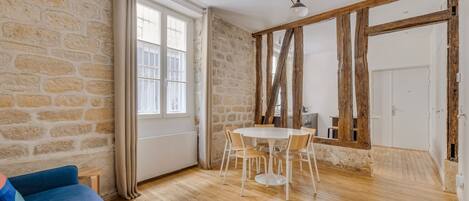 Una habitación con pared de piedra, piso de madera, una mesa redonda con sillas, un sofá azul y una puerta.