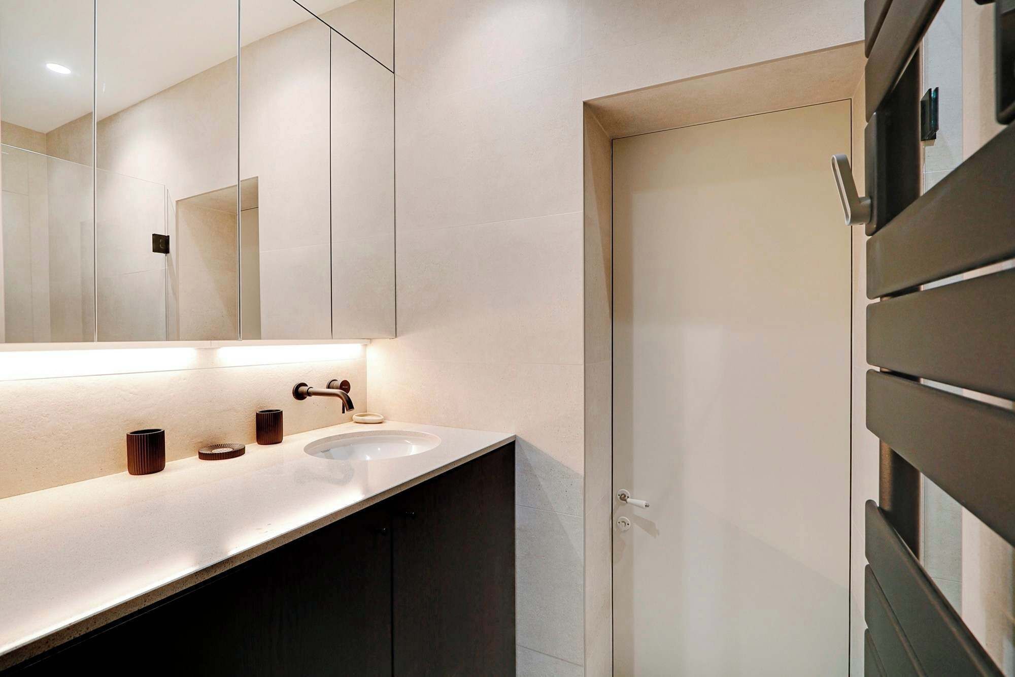 A modern bathroom with a large mirror, two sinks, and a dark-toned shower enclosure.