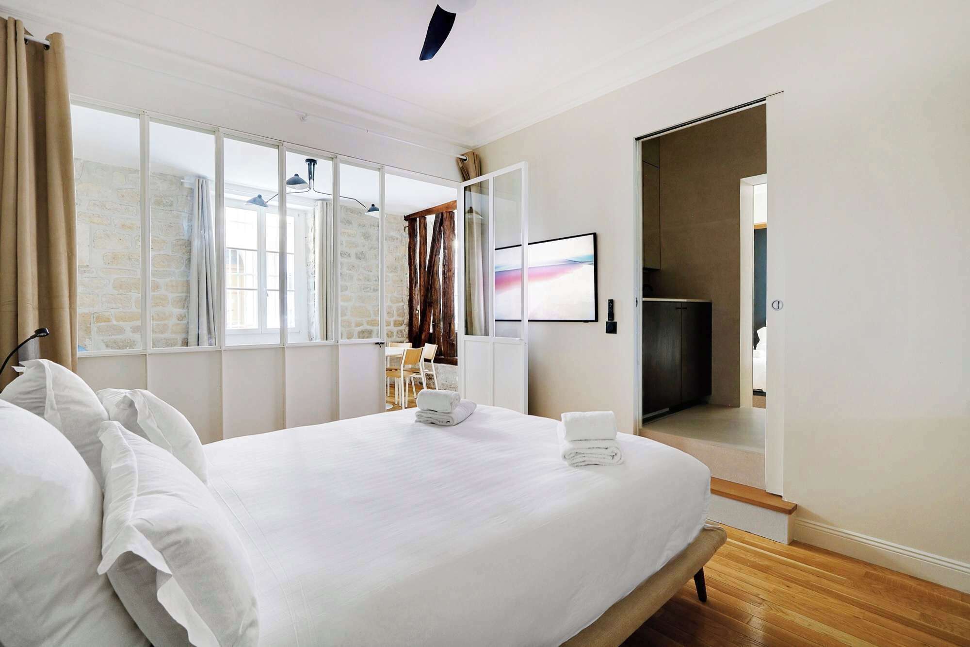Une chambre d’hôtel avec un grand lit, un coin repas avec des chaises, une télévision et une vue sur un mur en pierre.