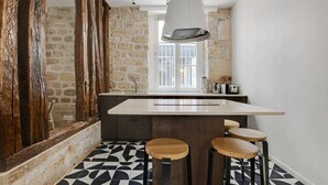 A kitchen with a stone wall, a large window, a hanging light fixture, and a bar area with stools. - A Stunning 2-BR in the 9th district- Folies (Paris)