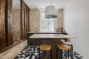 A kitchen with a stone wall, a large window, a hanging light fixture, and a bar area with stools. - A Stunning 2-BR in the 9th district- Folies (Paris)