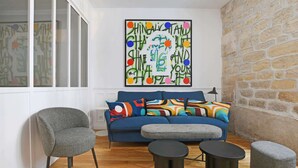 A modern living room with a blue sofa, grey armchairs, and a round coffee table. - A Stunning 2-BR in the 9th district- Folies (Paris)