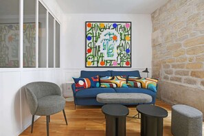 A modern living room with a blue sofa, grey armchairs, and a round coffee table. - A Stunning 2-BR in the 9th district- Folies (Paris)