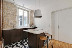 A kitchen with a stone wall, a window with white shutters, a modern pendant light, and a bar stool. - A Stunning 2-BR in the 9th district- Folies (Paris)