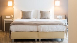 Ein Doppelbett mit einer neutralen Farbgestaltung, zwei Nachttische mit Lampen und ein Holzboden.