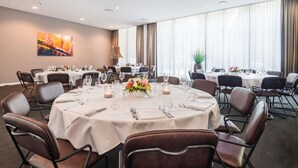 Ein Konferenzraum mit runden Tischen, Stühlen und einem großen Fenster mit Vorhängen.