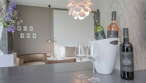 A hotel room with a bed, a bedside table with two wine glasses, a vase with flowers, and a bottle of Fletcher's Cuvée on the table. - Luxurious Suite w/Panoramic View | Stunning Outdoors & Historic Landmarks Nearby (Wageningen)