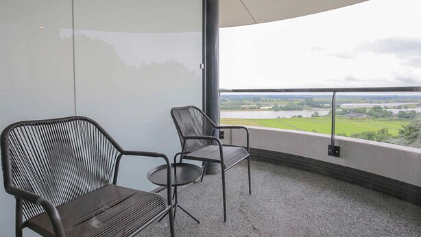 Een balkon met twee stoelen en uitzicht op een meer en velden.
