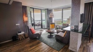 Una sala de estar moderna con un sofá, un sillón, una mesa de centro, ventanas amplias y vistas al exterior.