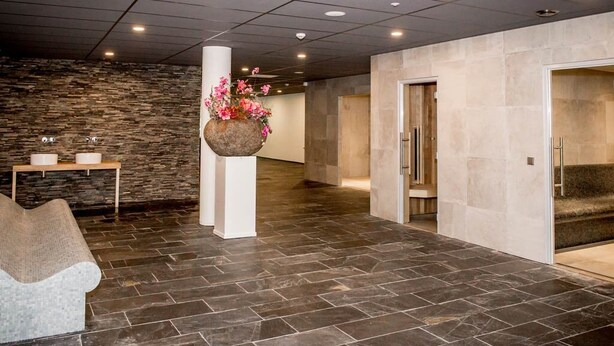 Un vestíbulo con suelo de piedra, una recepción, un arreglo floral colgante y una zona de estar.