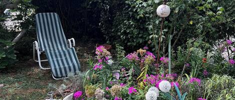 Un jardín con diversas plantas, una silla y un farol.
