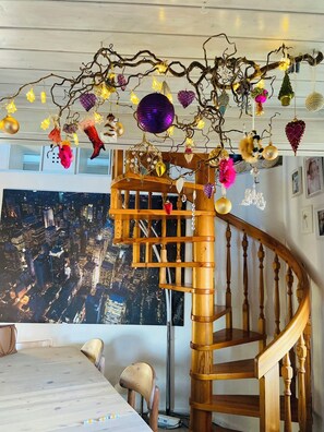 A spiral staircase with a wooden finish and ornate decorations, leading to a landing area with a cityscape view. - Familienurlaub nahe Europa-Park & Rulantica mit Garten, Trampolin & Balkon (Herbolzheim)
