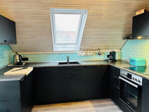 Pieni, käytännöllinen keittiö, jossa on ikkuna, pesuallas, liesi ja työtaso.