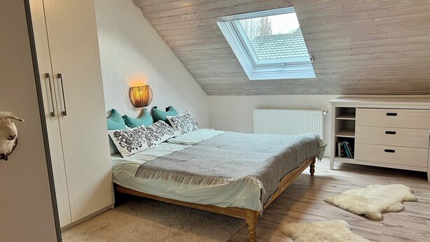 A bedroom with a sloped ceiling, a skylight, a bed with patterned bedding, a bedside lamp, a radiator, and a white dresser. - Familienurlaub nahe Europa-Park & Rulantica mit Garten, Trampolin & Balkon (Herbolzheim)
