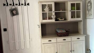 Ein Zimmer mit weißer Wand, Holzboden, einem weißen Schrank mit Glastüren und einem an der Wand befestigten Kleiderhaken.
