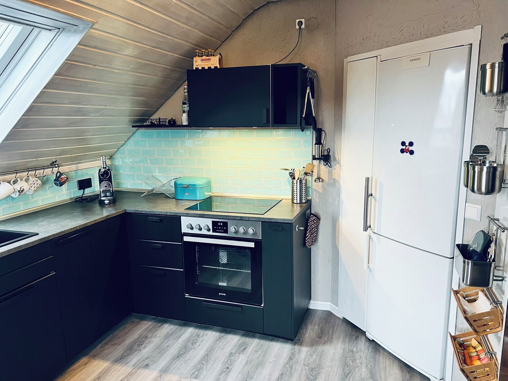 Eine kompakte Küche mit Einbauofen, einem weißen Kühlschrank und einem Fenster über der Spüle.