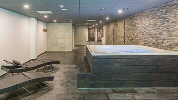 A spa area with a hot tub, lounge chairs, and a stone wall.