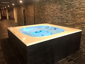 Banyera hidromassatge rectangular amb hidrojet, davant d'una paret de pedra en un espai interior ben il·luminat.