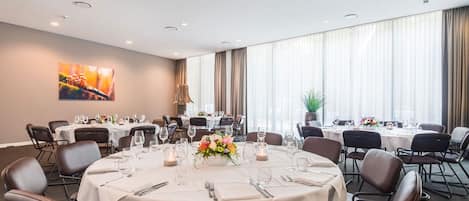 A conference room with round tables, chairs, and a large window with curtains.
