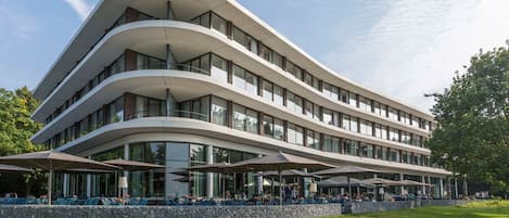 A modern multi-story building with a curved facade, outdoor seating area, and a stone retaining wall.