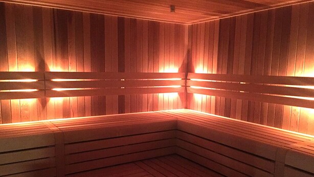 En sauna med træbænke og vægge, oplyst af varm belysning.