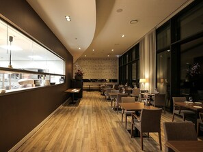 Moderni ravintola, jossa on puulattiat, suuret ikkunat ja erilaisia istumajärjestelyjä.