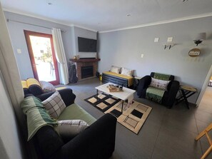 A living room with a sofa, a coffee table, a fireplace, and a television. - Charming 3-bedroom House Rental in White River, South Africa (Mbombela)