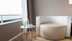 A modern room with a round ottoman, a small table with a vase and glasses, and a window with a view. - Family Friendly Nature Escape w/Dining & Spa | Nature Reserves & Local Landmarks (Wageningen)