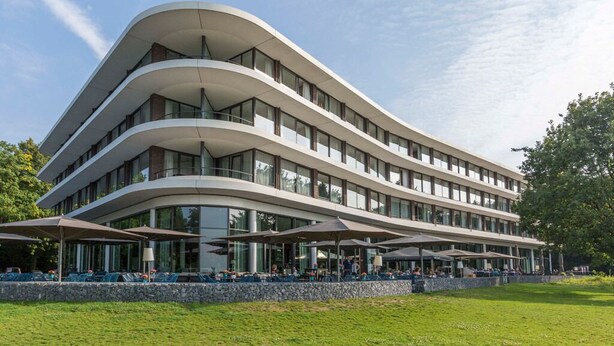 Um edifício moderno de vários andares com fachada curva, área de estar ao ar livre e um muro de pedra de contenção.