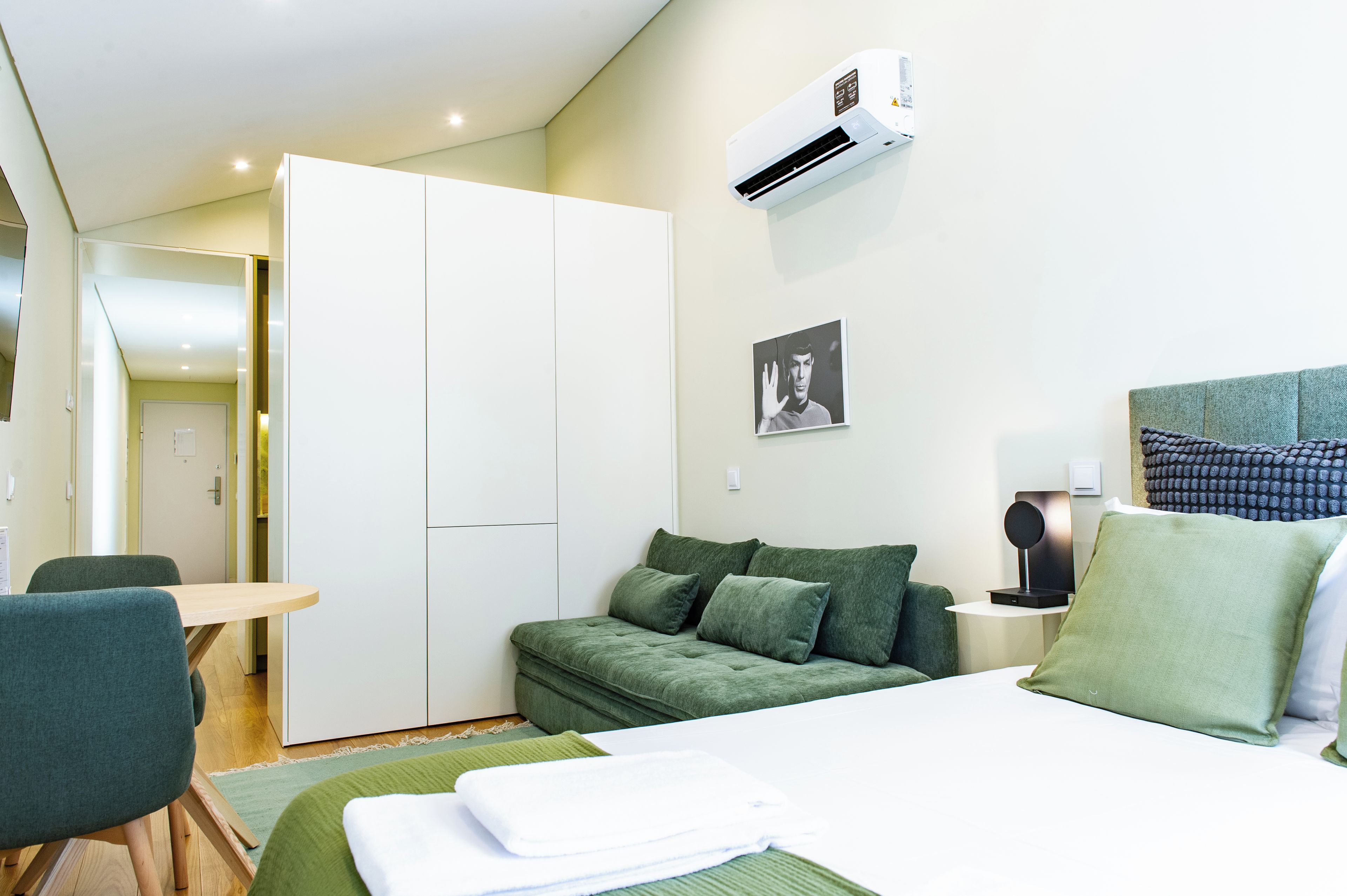 Une chambre d’hôtel moderne avec un lit, un canapé vert et un bureau.