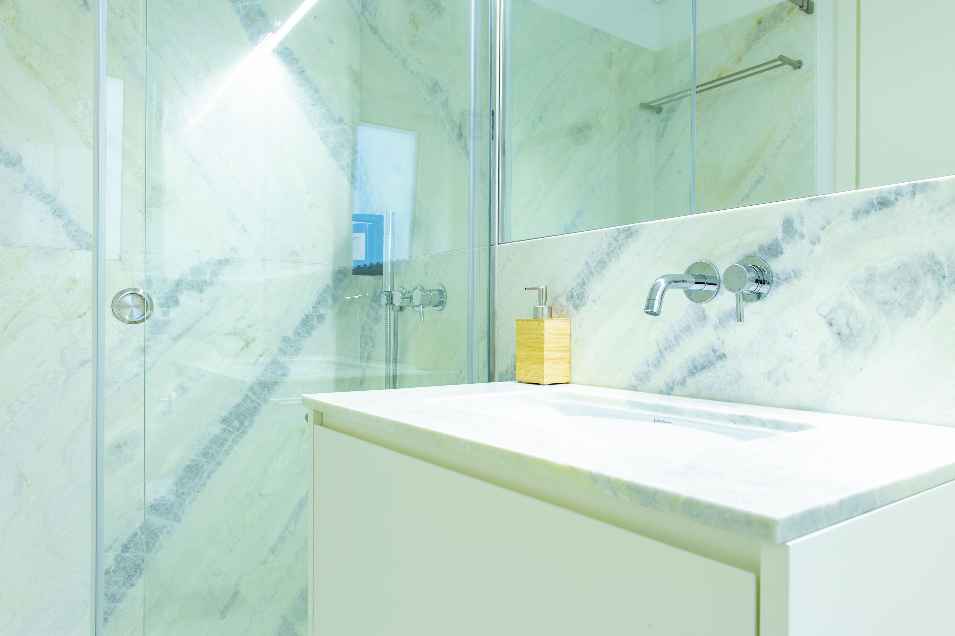 A bathroom with a glass shower enclosure, a white sink, and a mirror.