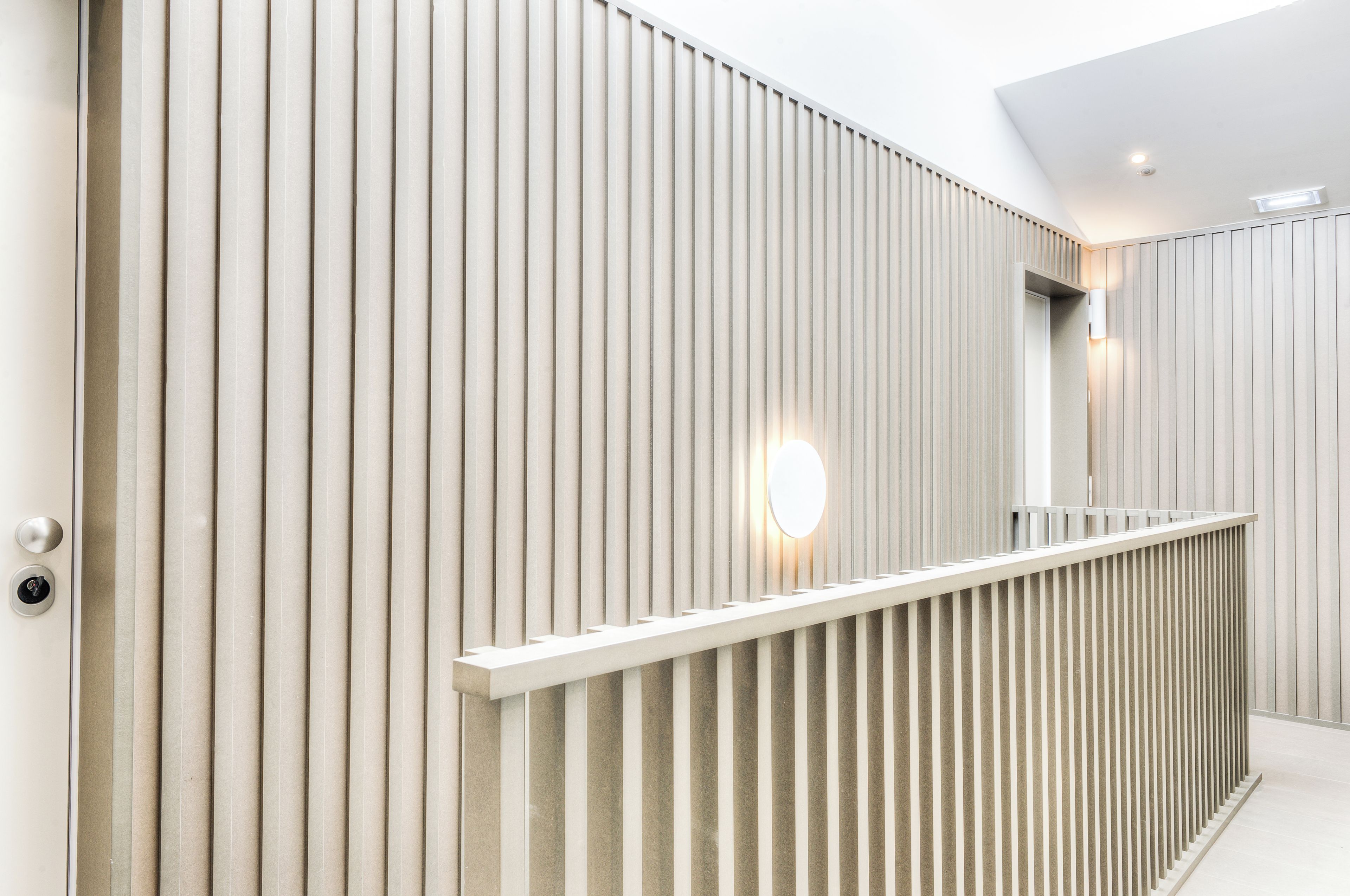 A modern interior with vertical paneling, a white railing, and a round light fixture.