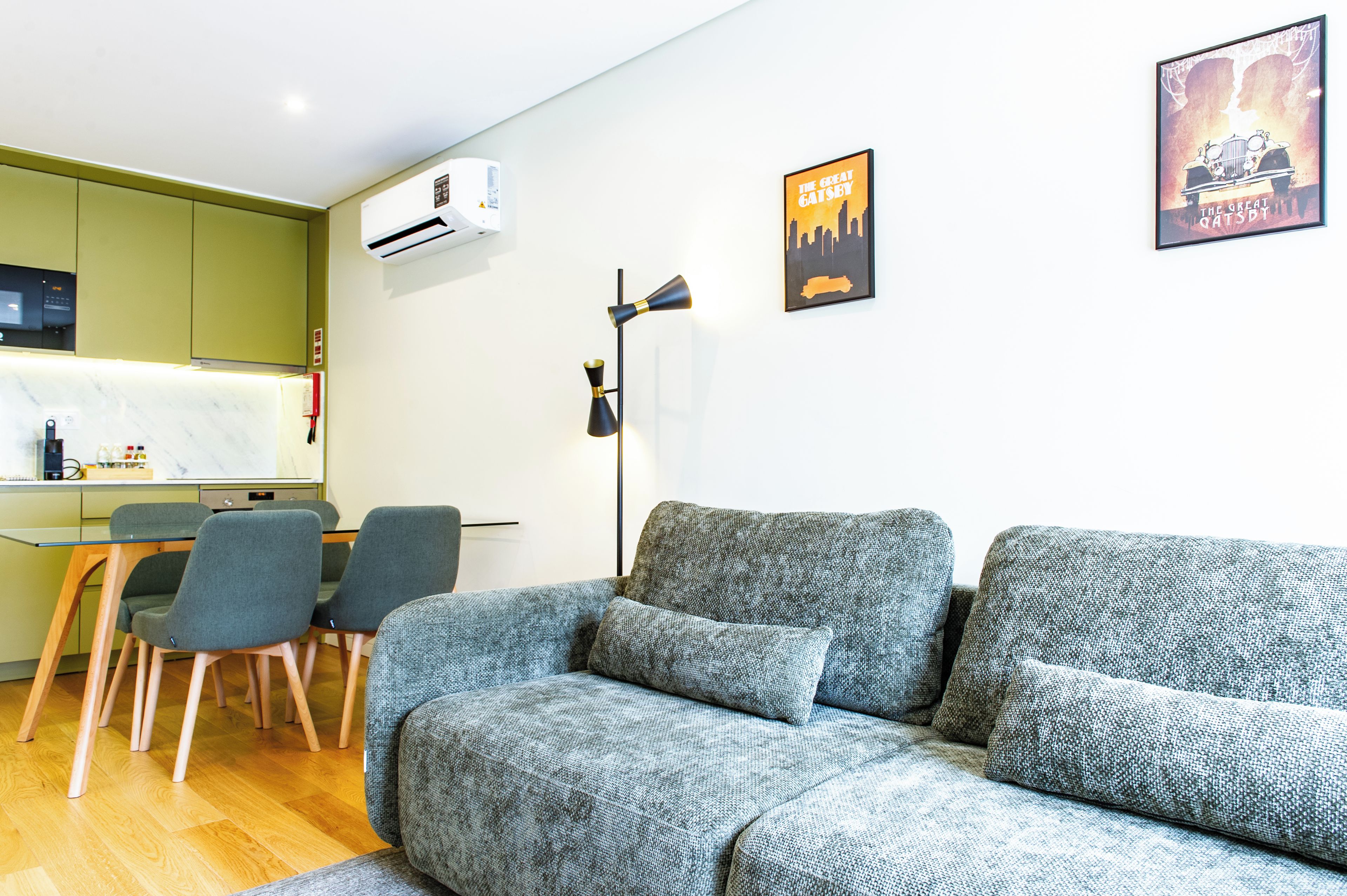 Ein modernes Wohnzimmer mit einem grauen Sofa, einem Essbereich mit Stühlen und zwei Wand-Klimageräten.