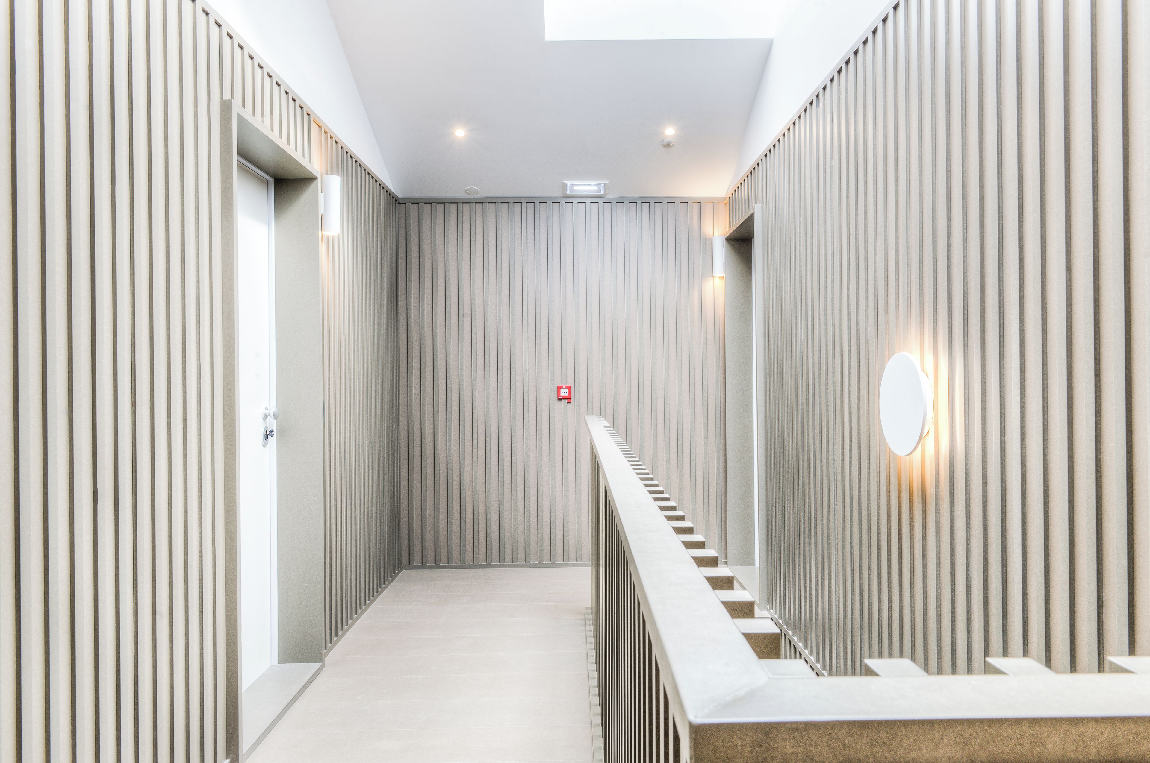 A modern interior with a straight staircase, recessed lighting, and a plain wall with vertical lines.