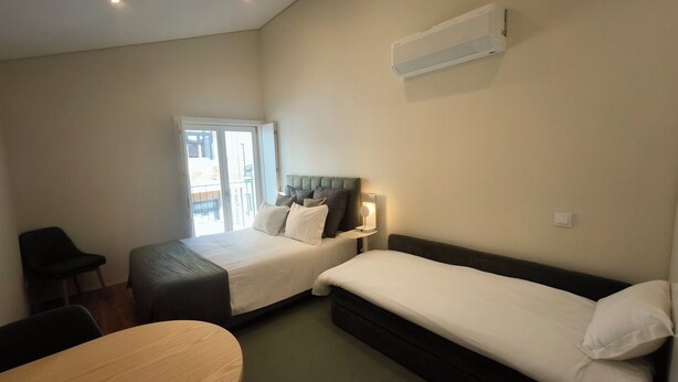 A hotel room with two beds, a desk, a chair, and an air conditioning unit on the wall. - Carmo Cinema Apartments (Porto)