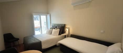Une chambre d’hôtel avec deux lits, un bureau, une chaise et un appareil de climatisation fixé au mur.