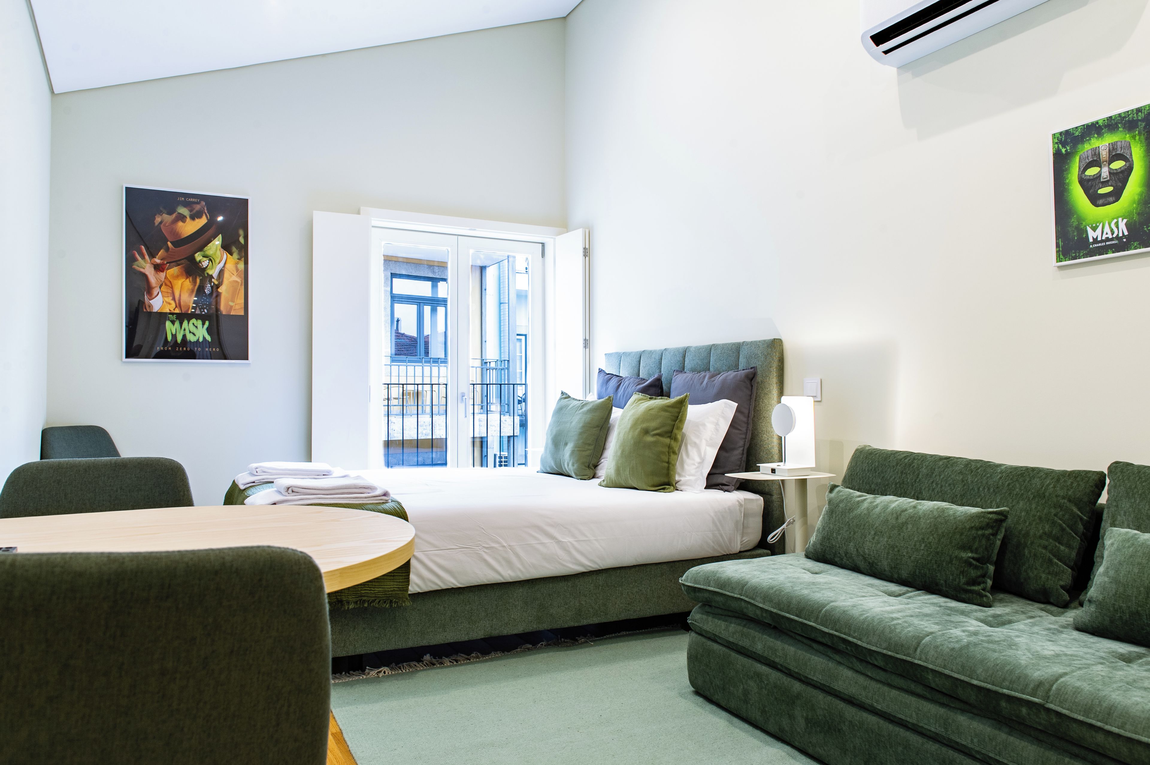 A hotel room with a bed, a green sofa, a table with towels, and a poster on the wall.