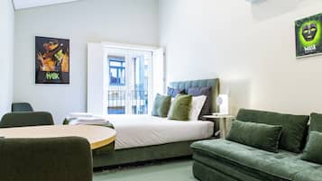 Une chambre d’hôtel avec un lit, un canapé vert, une table avec des serviettes et une affiche au mur.