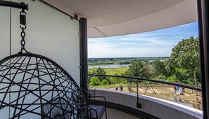 Ein Balkon mit einer Hängematte, Blick auf einen Fluss und ein Spielplatz.