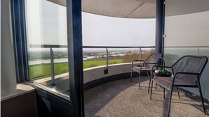 Uma varanda com vista para um rio e campos, uma cadeira e uma mesa pequena.