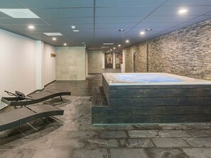 A spa area with a hot tub, lounge chairs, and a stone wall.