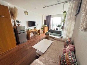 Ein kompakter Wohnbereich mit Küchenzeile, einer Couch mit gemusterten Kissen, einem Essbereich mit Tisch und Stühlen sowie einem an der Wand befestigten Fernseher.
