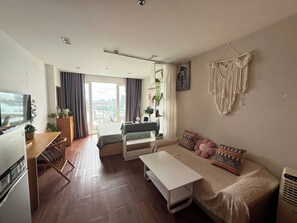 Ein modernes Wohnzimmer mit einer Couch, einem Couchtisch, einem Fernseher und einem Balkon mit Vorhängen.