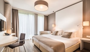 Hotellihuone, jossa on sänky, yöpöydät, työpöytä tuolilla, televisio ja suuri ikkuna, jossa on verhot.