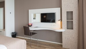 Moderni hotellihuone, jossa on työpöytä, tuoli ja suuri peili.