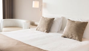 Een hotelkamer met een bed, twee kussens, een stoel, een nachtkastje en een lamp.