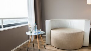 Quarto moderno com um banquinho redondo, uma mesinha com um vaso e copos, e uma janela com vista.