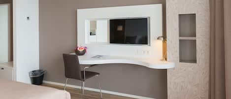 A modern hotel room with a desk, chair, and a large mirror.