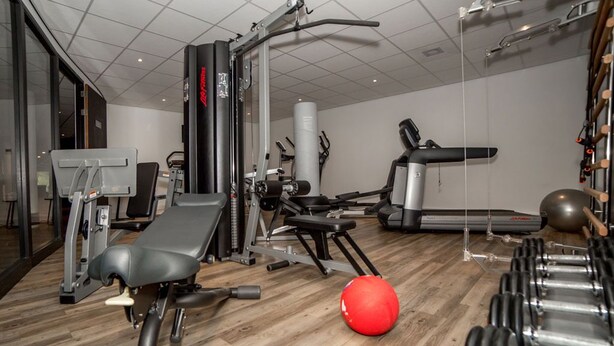 Uma academia com equipamentos de ginástica, um banco, uma bola de exercício vermelha e halteres.