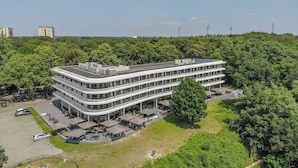 Um edifício de vários andares com telhado plano, rodeado por vegetação.